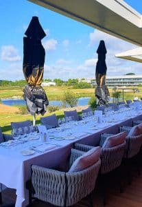 golf-roissy-evenementiel-Terrasse-Aula-Magna Photo d'une table dressée sur une terrasse au soleil, illustrant l'originalité du UGOLF Roissy, lieu événementiel Paris